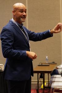 A man in a suit gestures with his left hand
